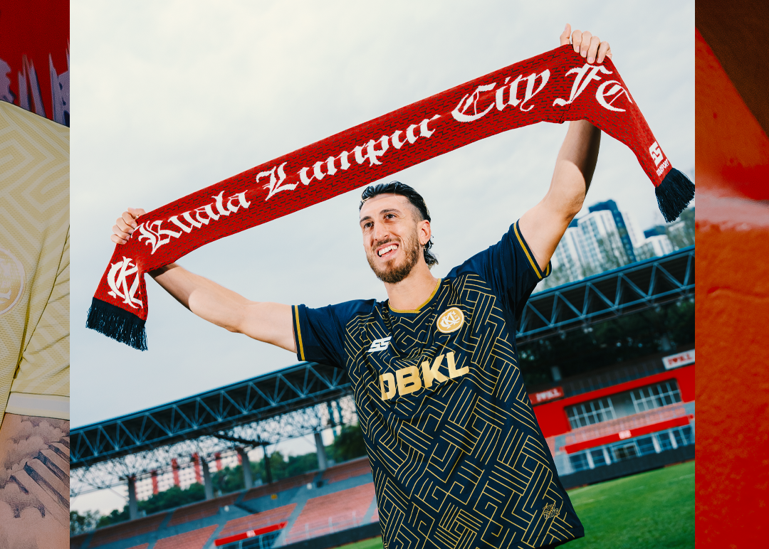 Person wearing a sports jersey and holding a scarf with text, standing on a sports field.